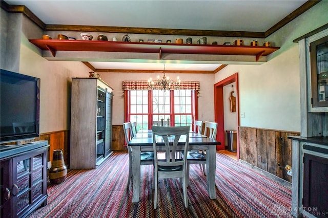 dining space with wooden walls, a chandelier, a wainscoted wall, and wood finished floors