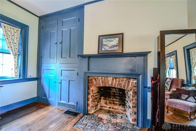 details with visible vents, wood finished floors, baseboards, and a brick fireplace