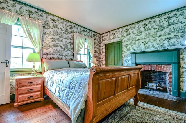 bedroom featuring a fireplace, ornamental molding, dark wood-style floors, and wallpapered walls