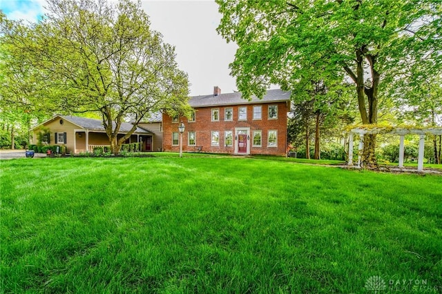 rear view of property with a yard, a pergola, brick siding, and a chimney