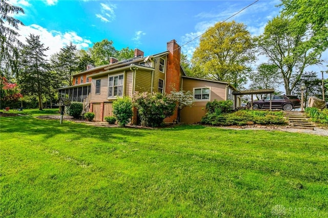 rear view of property featuring stairs, a carport, a chimney, and a lawn