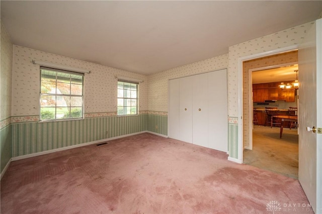 unfurnished bedroom with a chandelier, carpet, wallpapered walls, visible vents, and a closet