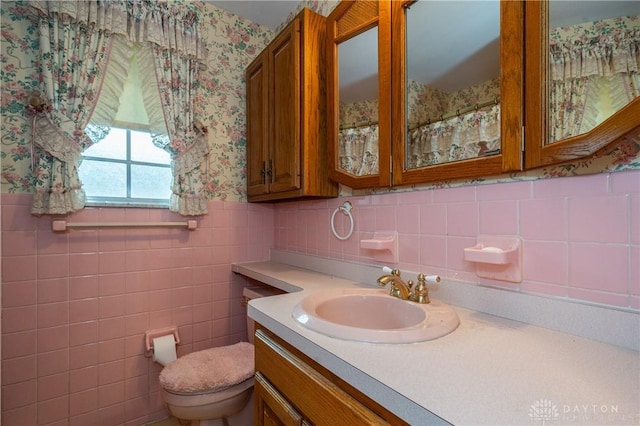 bathroom with vanity, wainscoting, toilet, tile walls, and wallpapered walls