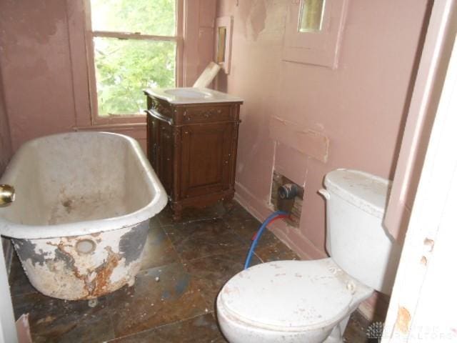 bathroom featuring toilet, a freestanding tub, baseboards, and vanity
