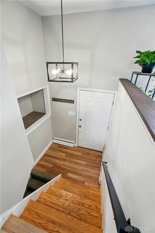 staircase featuring an inviting chandelier, baseboards, a baseboard heating unit, and wood finished floors
