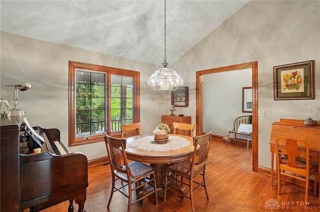 dining area with baseboards, an inviting chandelier, light wood-style flooring, and lofted ceiling