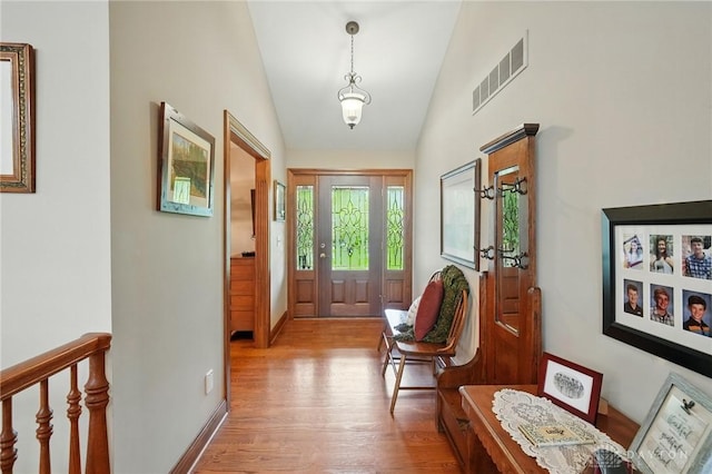 doorway with baseboards, lofted ceiling, light wood finished floors, and visible vents