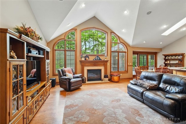 living room featuring recessed lighting, light wood-style flooring, a glass covered fireplace, and vaulted ceiling