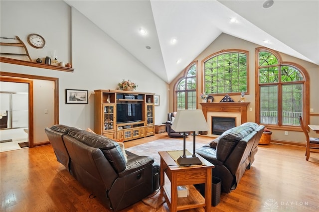 living room with high vaulted ceiling, a glass covered fireplace, recessed lighting, baseboards, and wood finished floors