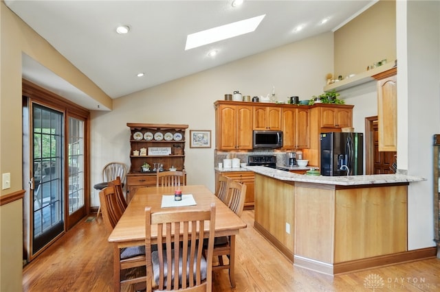 kitchen featuring decorative backsplash, a skylight, stainless steel microwave, light wood finished floors, and black refrigerator with ice dispenser