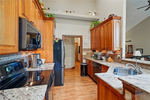 kitchen featuring light stone countertops, appliances with stainless steel finishes, a sink, light wood-style flooring, and a ceiling fan