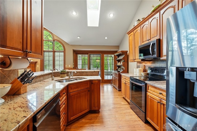 kitchen featuring light stone countertops, a sink, light wood-style floors, stainless steel appliances, and tasteful backsplash
