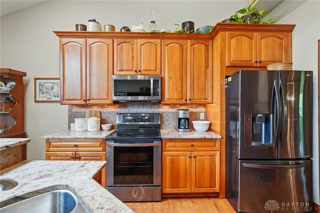 kitchen with light stone counters, decorative backsplash, appliances with stainless steel finishes, and light wood-type flooring