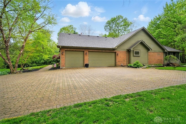 ranch-style home featuring brick siding, an attached garage, a shingled roof, and decorative driveway