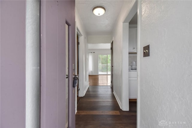 corridor featuring baseboards, a textured wall, and dark wood-type flooring