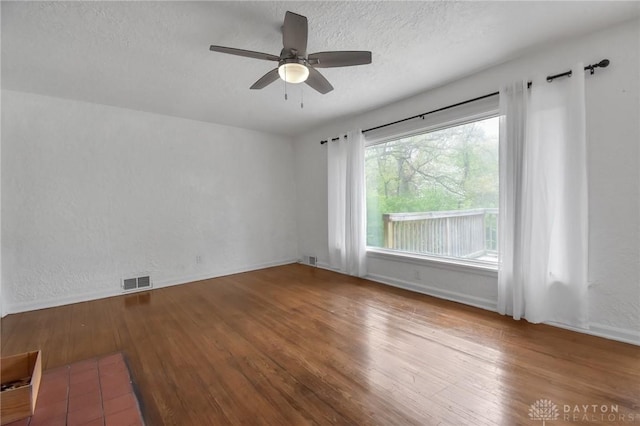 empty room with a textured ceiling, ceiling fan, wood finished floors, and visible vents