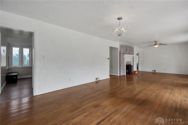 unfurnished living room featuring a fireplace, a textured ceiling, ceiling fan with notable chandelier, visible vents, and hardwood / wood-style flooring