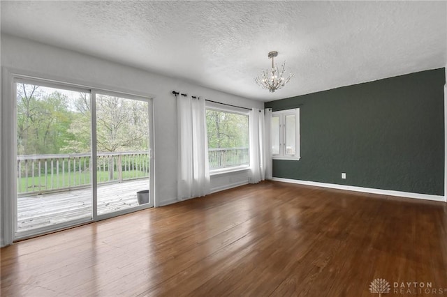spare room with baseboards, a textured ceiling, wood finished floors, and a notable chandelier