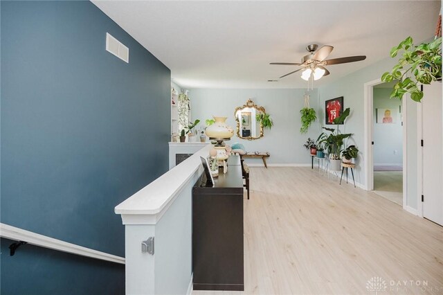 interior space featuring light wood-type flooring, baseboards, visible vents, and an upstairs landing