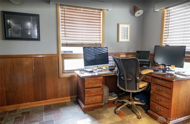 office space featuring wainscoting, wood walls, and stone tile floors