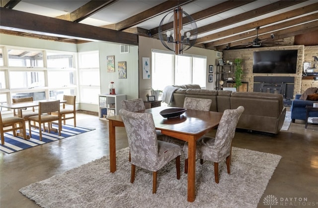 dining room with visible vents, finished concrete flooring, a large fireplace, ceiling fan with notable chandelier, and vaulted ceiling with beams