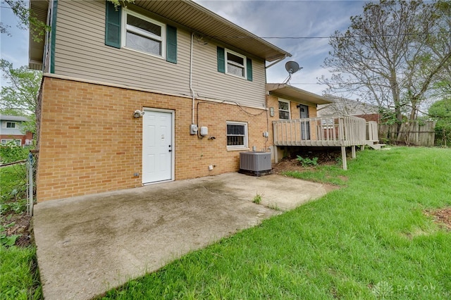 rear view of property with brick siding, a deck, cooling unit, a patio area, and a yard