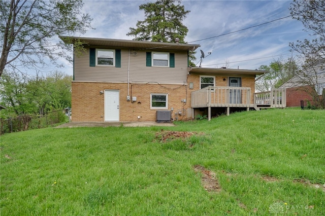 rear view of house with central air condition unit, brick siding, a yard, and a wooden deck