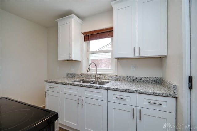 kitchen featuring a sink, white cabinets, light stone countertops, and black electric range