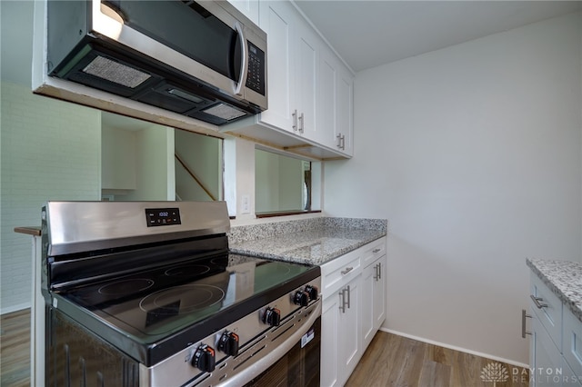 kitchen featuring white cabinets, stainless steel appliances, light stone counters, and light wood-style floors