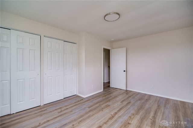 unfurnished bedroom with baseboards, wood finished floors, and two closets