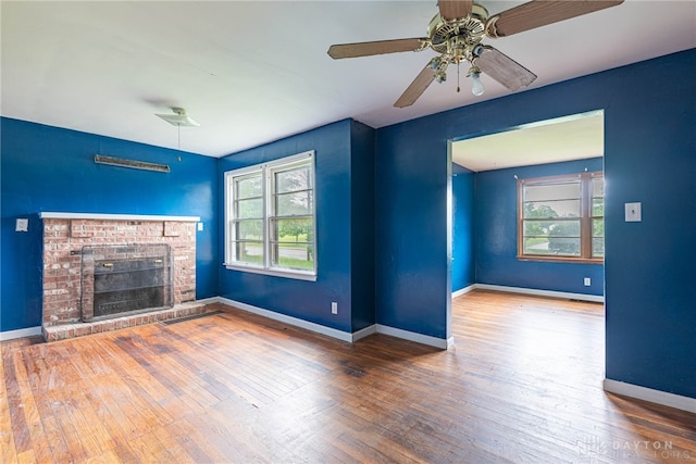 unfurnished living room with a healthy amount of sunlight, baseboards, a brick fireplace, and hardwood / wood-style floors