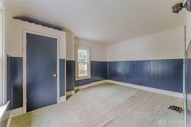 unfurnished room with wooden walls, a wainscoted wall, carpet flooring, and visible vents