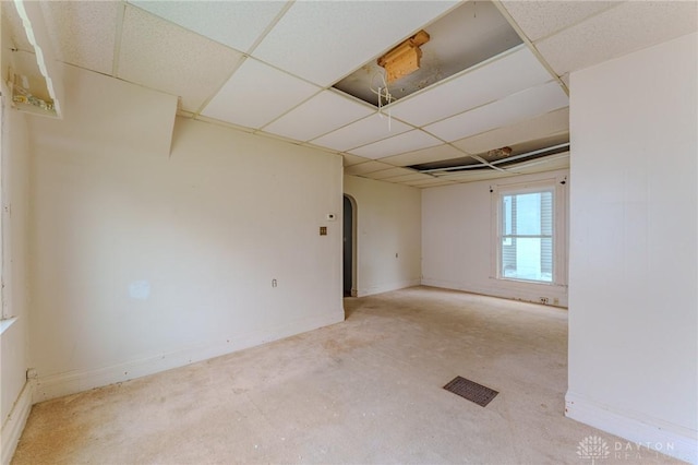 spare room featuring visible vents, arched walkways, baseboards, and a drop ceiling