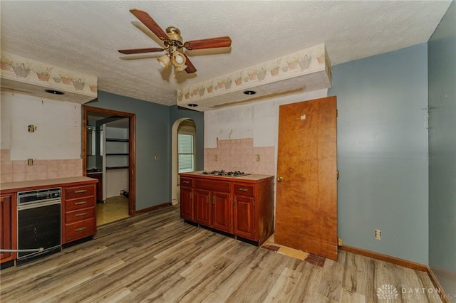 kitchen featuring light wood-style floors, stainless steel gas cooktop, arched walkways, a ceiling fan, and decorative backsplash