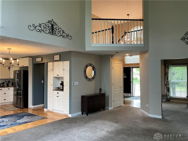 unfurnished living room featuring an inviting chandelier, baseboards, light colored carpet, and a towering ceiling
