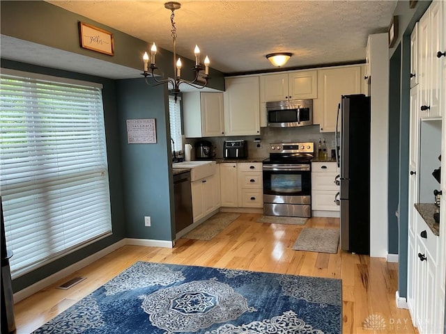 kitchen with backsplash, appliances with stainless steel finishes, light wood-type flooring, white cabinets, and a chandelier