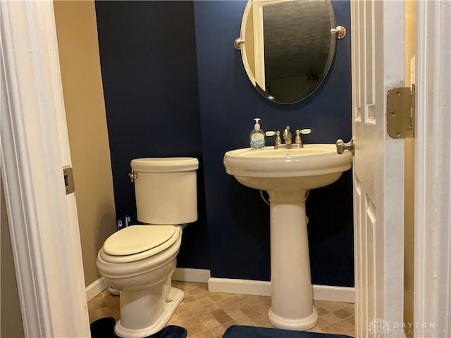 half bath featuring baseboards and toilet