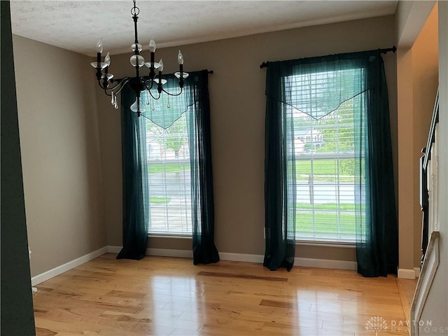 unfurnished dining area with baseboards, plenty of natural light, light wood-style flooring, and a chandelier