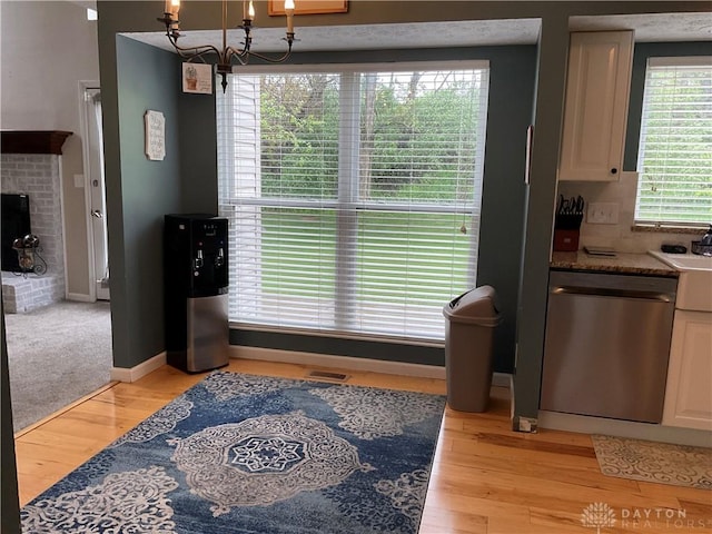 kitchen featuring a notable chandelier, stone countertops, light wood-type flooring, stainless steel dishwasher, and visible vents