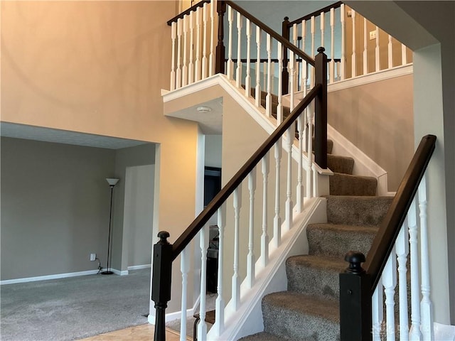 stairway with carpet flooring, a high ceiling, and baseboards