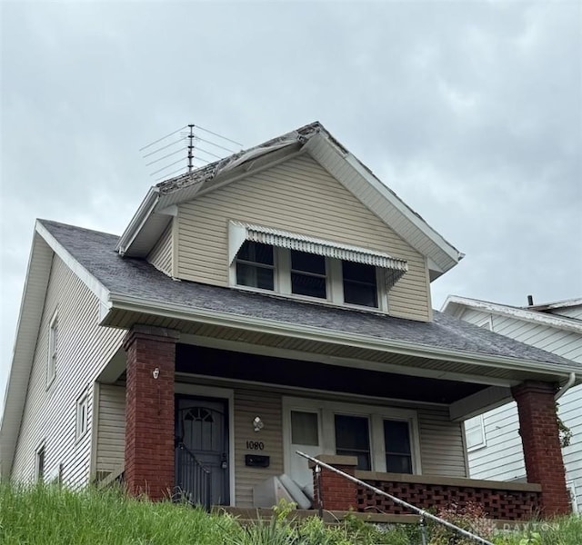 view of front of home featuring covered porch, brick siding, and a shingled roof