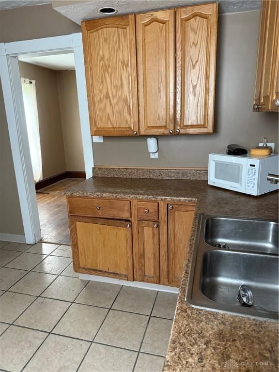 1080 Linden Ave, Dayton, OH 45410 - kitchen with white microwave, light tile patterned floors, a sink, dark countertops, and baseboards