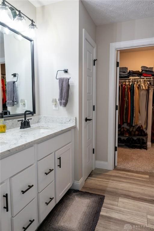 bathroom featuring vanity, baseboards, wood finished floors, and a spacious closet