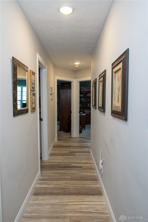 hallway with a textured ceiling, baseboards, and light wood-style flooring