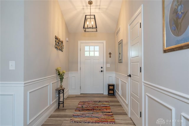 doorway with visible vents, wainscoting, wood finished floors, a notable chandelier, and a decorative wall