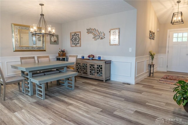 dining room featuring light wood finished floors, a wainscoted wall, and a notable chandelier