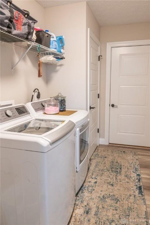 laundry area featuring washing machine and clothes dryer, a textured ceiling, laundry area, and light wood-style flooring
