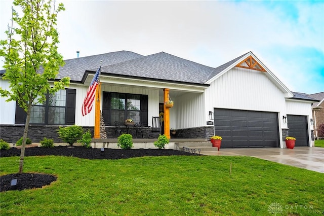 view of front facade with a shingled roof, an attached garage, a front lawn, stone siding, and concrete driveway