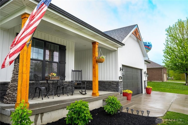view of side of home featuring roof with shingles, stone siding, a garage, concrete driveway, and covered porch
