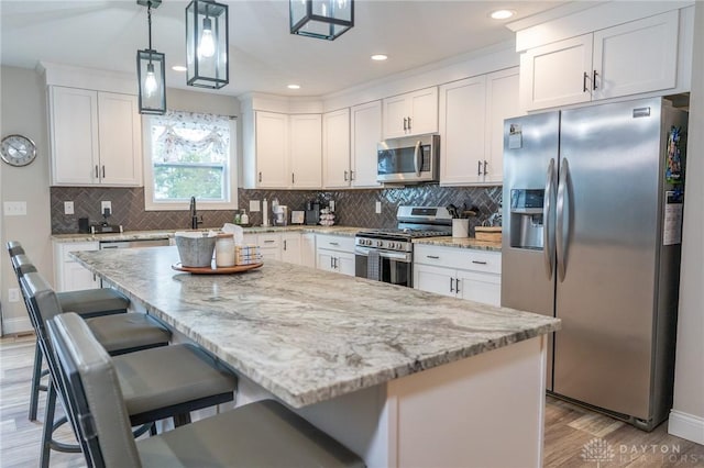 kitchen with light stone counters, white cabinets, stainless steel appliances, and light wood-type flooring